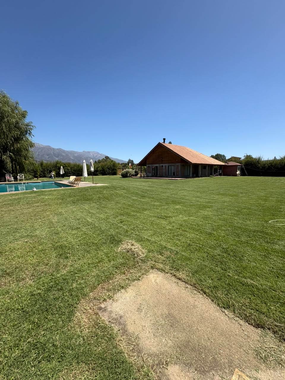 Césped recién cortado en parcela con piscina y cordillera