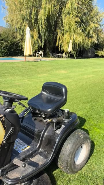 Tractor cortacésped en un parque con piscina
